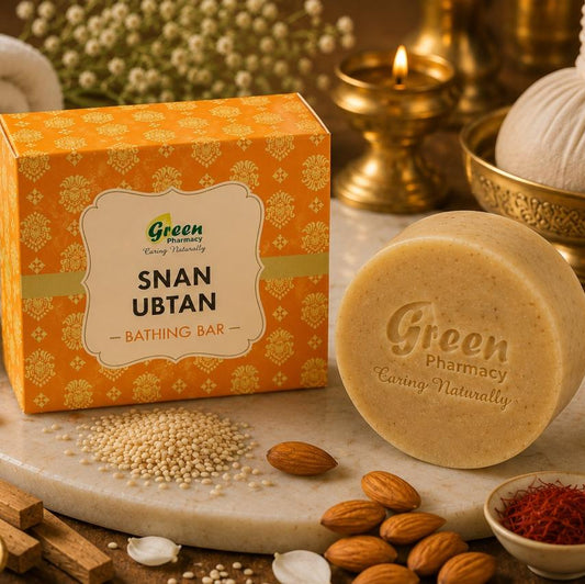 A bath bar product display featuring a round beige bath bar labeled 'Green Pharmacy Snan Ubtan' next to its orange patterned box, styled with almonds, spices, flowers, and traditional bath accessories on a marble surface.